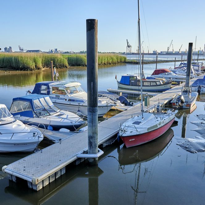 Boote im Hafen in Sandstedt an der Unterweser bei Niedrigwasser. Im Hintergrund sind Kräne zu sehen.