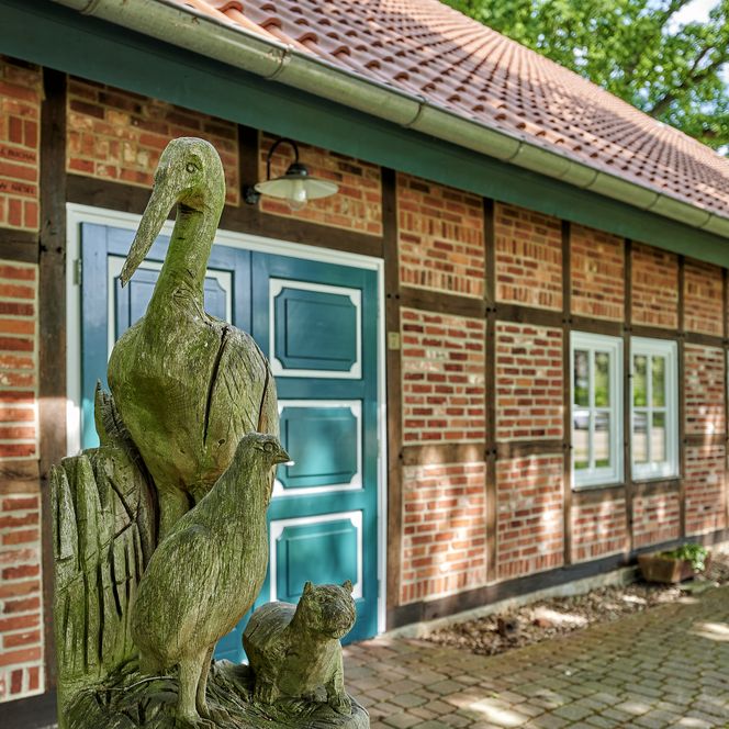 Das Dorphuus in Beverstedt an einem Sommertag. Im Vordergrund sieht man eine Schnitzfigur aus Holz.