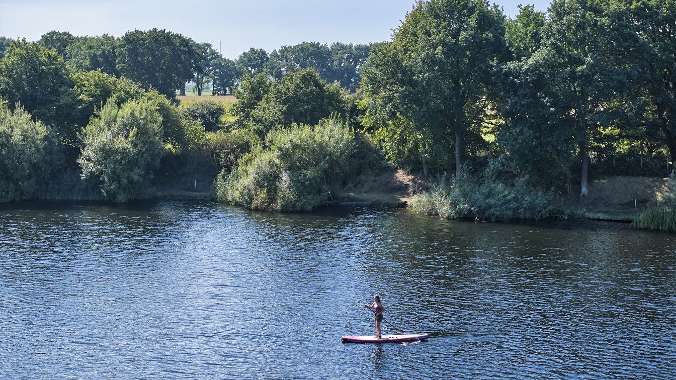 Standup-Paddlerin auf einem See. Im Hintergrund sieht man das Ufer.
